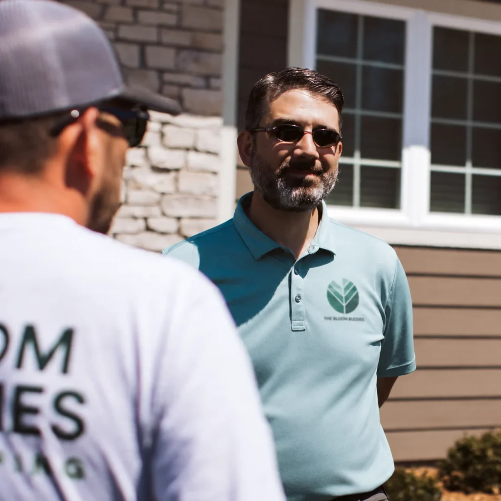 Landscape business owner speaking with a team member outside a residential property, reflecting hands-on leadership and field operations.